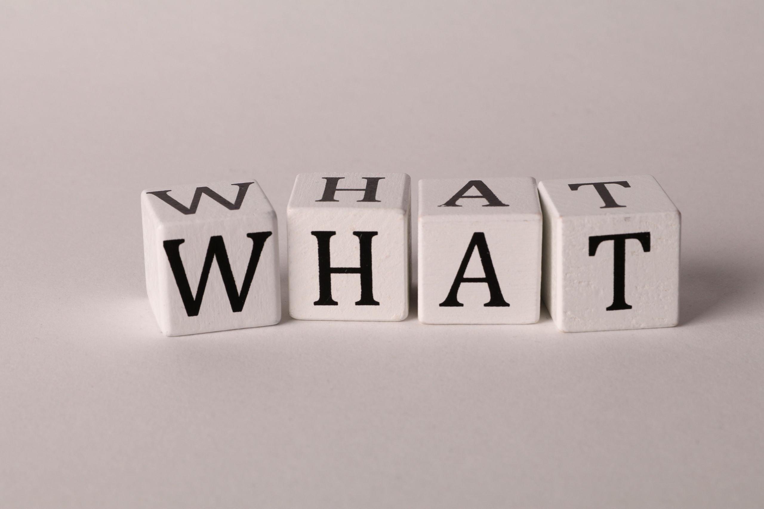 Close-up of wooden blocks with letters spelling 'What' on a white background, emphasizing curiosity and inquiry.